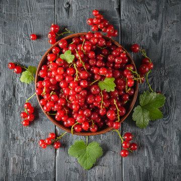 Freshly picked redcurrant berries in a clay bowl on a dark wooden table. Flat lay.