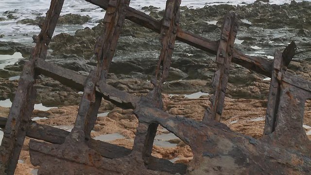Remaining framework of a ship wreck's hull stranded on a rocky beach with calm waves in the background