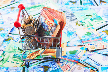 Tenge. A pack of Kazakh banknotes in a shopping cart on the background of a pile of money. Close up..