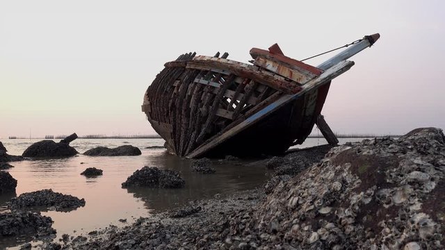 Dolly shot of shipwreck on the rocky beach in beautiful sunset background.