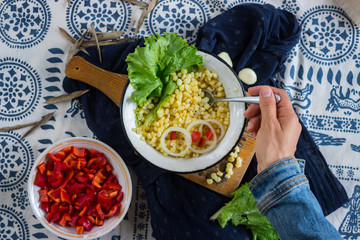 Woman hands holds sweet white corn or yellow corn cooked. Tasting grains cut into metal bowl. Vegetarian lunch. Vegan dinner. Healthy food. Served with green salad leaves.