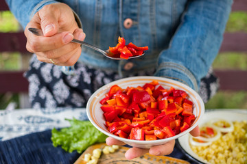Woman hands holds red bell pepper salad with unrefined sunflower oil, rock salt, black pepper and pieces of tomatoes. Raw vegan lunch with capsicum and vegetarian dinner food.