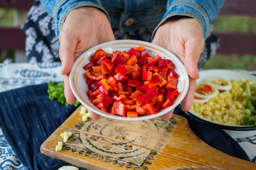Woman hands holds red bell pepper salad with unrefined sunflower oil, rock salt, black pepper and pieces of tomatoes. Raw vegan lunch with capsicum and vegetarian dinner food.