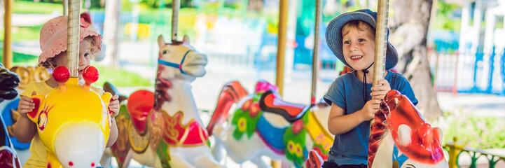 Cute little boy and girl enjoying in funfair and riding on colorful carousel house BANNER, long format © galitskaya