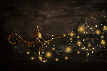 Image of magical mysterious aladdin lamp with glitter sparkle lights over black background. Lamp of wishes.