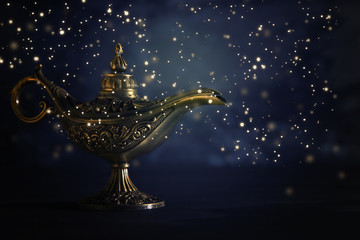 Image of magical mysterious aladdin lamp with glowing glitter lights over black background. Lamp of...