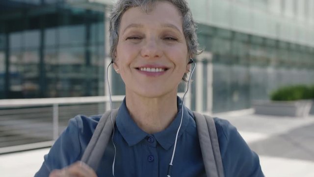 portrait of mature confident business woman smiling happy puts on earphones listening to music enjoying leaving work 