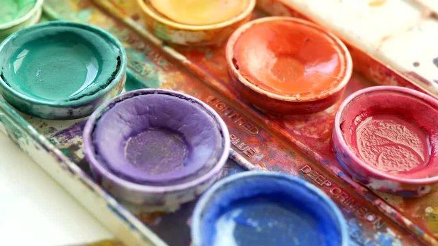 Artists dipping wet paintbrush into orange watercolor ORBIT
