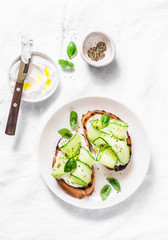 Labne and pickled cucumbers toast on a light background, top view. Sandwiches with soft cheese and cucumber - delicious healthy breakfast, snack. Flat lay