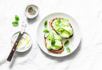 Labne and pickled cucumbers toast on a light background, top view. Sandwiches with soft cheese and cucumber - delicious healthy breakfast, snack. Flat lay