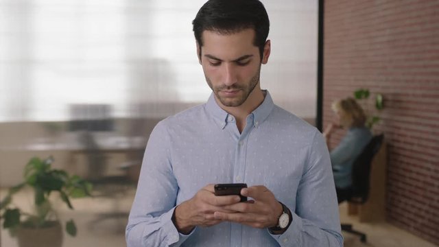 portrait of young handsome middle eastern businessman texting browsing using smartphone mobile technology checking messages in office workspace