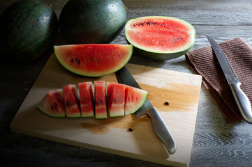 Watermelon slices on chopping board and knife all on wooden table in dim light