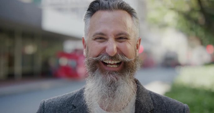 portrait of confident businessman with beard laughing cheerful enjoying successful urban lifestyle mature male entrepreneur wearing stylish fashion in city street background slow motion