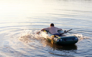 Fisherman rowing a rubber boat on the river