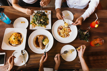 Group of male and female friends having dinner and eating steak and salad and spaghetti together in restaurant  - top view.