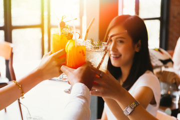 Beautiful and cheerful Asian woman cheering up for toast and celebration with friends in bar - focus on glasses.