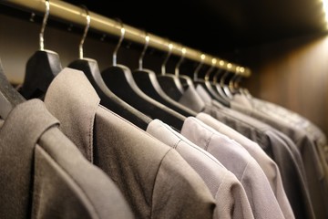 modern wooden wardrobe with clothes hanging on rail in walk in closet, Choice of fashion clothes of different colors on wooden hangers
