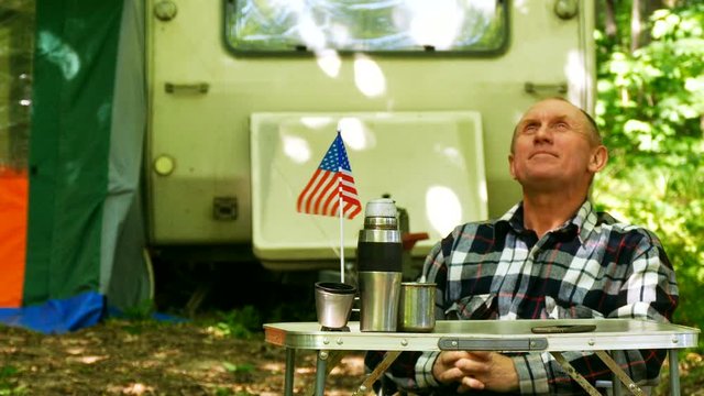 4K.Man traveler with trailer   sit  at table with American flag in wood 

