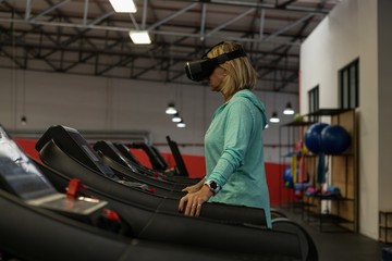 Mature woman using virtual reality headset while exercising on