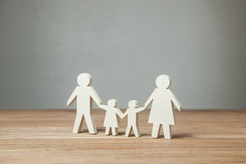 Family symbol, father, mother, daughter and son hold hands on wooden table