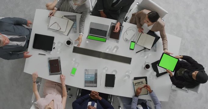 multi ethnic business people brainstorming innovative ideas viewing chroma key using mobile computer technology in boardroom meeting overhead