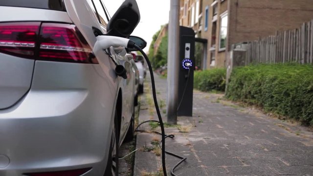 An electric car charging in a parkinglot next to the pavement.