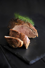 Fillet of meat on a black board and fresh greens.