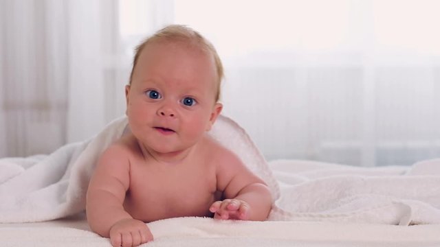 Adorable little baby with cute blue eyes lies on belly and smiling
