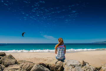  girl is sitting on the ocean. Woman sits back and looks at the sea. Kite surfing. Active rest on the beach. Kitesurfing. paragliding on the waves   © NatBud