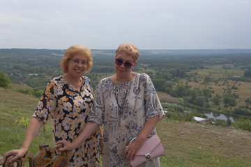 Two mature women stand against the background of a panoramic view