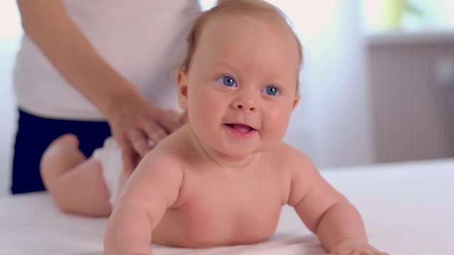 Adorable newborn baby with beautiful blue eyes lies on belly while mother giving a massage