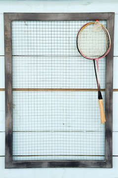 Bandminton rackets on a black net on a blue painted wood background