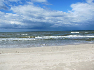 The shore of a calm sea, an empty beach and a huge blue sky with white clouds, spaciousness, air, peace