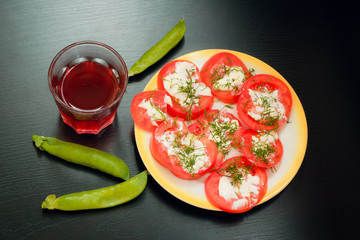 Sliced tomatoes covered with cheese on a plate on a dark table