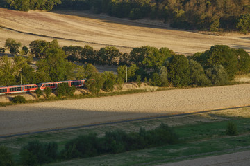 red train rides through a beautiful rolling hills in the fields with wheat in the rays of the evening sun.