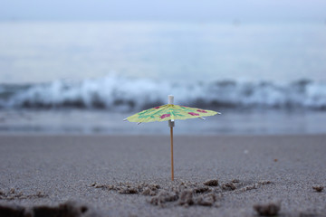 An umbrella from a cocktail in the sand on the beach against the background of sea waves. Concept,...
