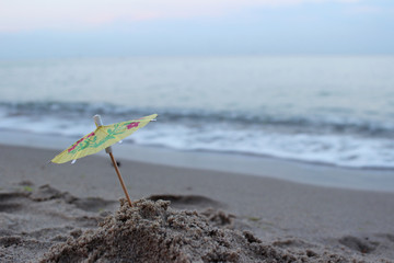 An umbrella from a cocktail in the sand on the beach against the background of sea waves. Concept,...