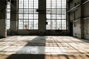 alte Fabrikshalle mit sehr hohen Fenstern, Licht wirft Schatten der Fenster auf den Boden