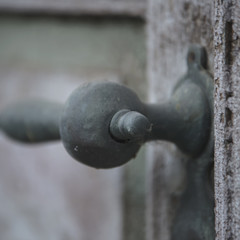 Old rusty front door handle close-up on a wooden door with cracked paint.