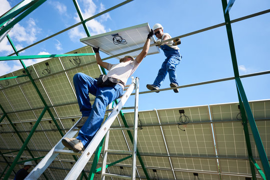 Workers mounting solar batteries on metallic construction. risky work for professionals. Modern solution for natural resources saving, using renewable solar energy. Environment friendly, green energy.