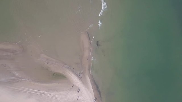 Topview from drone flying over the ocean of Grenen, Denmark. This is where the North Sea and the Baltic Sea meet. People standing on the northernmost point of Grenen.