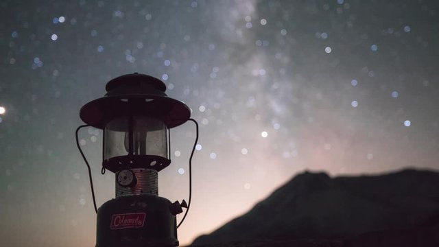 Vintage Coleman latern in focus while the Milky Way moves across the screen.