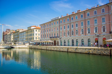Obraz premium Italian old city street alley way with small river stream canal between buildings facade in bright colorful summer morning time and blue sky background