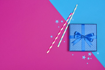 Blue classic gift box with shiny satin bow and paper striped cocktail straws with confetti in the shape of stars as attributes of party