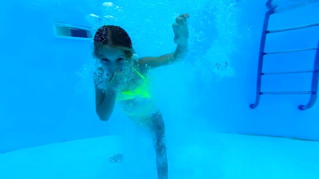 Little girl diving under the water in swimming pool and showing thumbs up sign. Young teen girl in yellow swimsuit in the waterpool. Girl plunging in the water