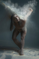 Fototapeta na wymiar Dancing in flour concept. Muscle fitness guy man male dancer in dust / fog. Guy wearing white shorts making dance element in flour cloud on isolated grey / black background