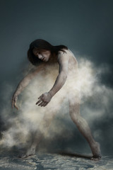 Dancing in flour concept. Muscle fitness guy man male dancer in dust / fog. Guy wearing white shorts making dance element perfomance in flour cloud on isolated grey / black background