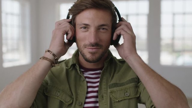 close up portrait of attractive young man smiles at camera puts on headphones listening to music enjoying leisure activity in apartment