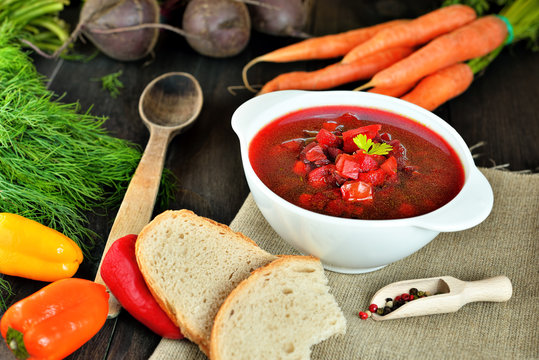 Healthy Borscht. National Ukrainian and Russian red soup made of beetrot and vegetables on a dark, wooden, rustic table with ingredients. Colorful concept photo of Traditional Ukraine food cuisine