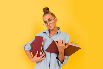 young girl in round glasses and with books in her hands smiling on a yellow background